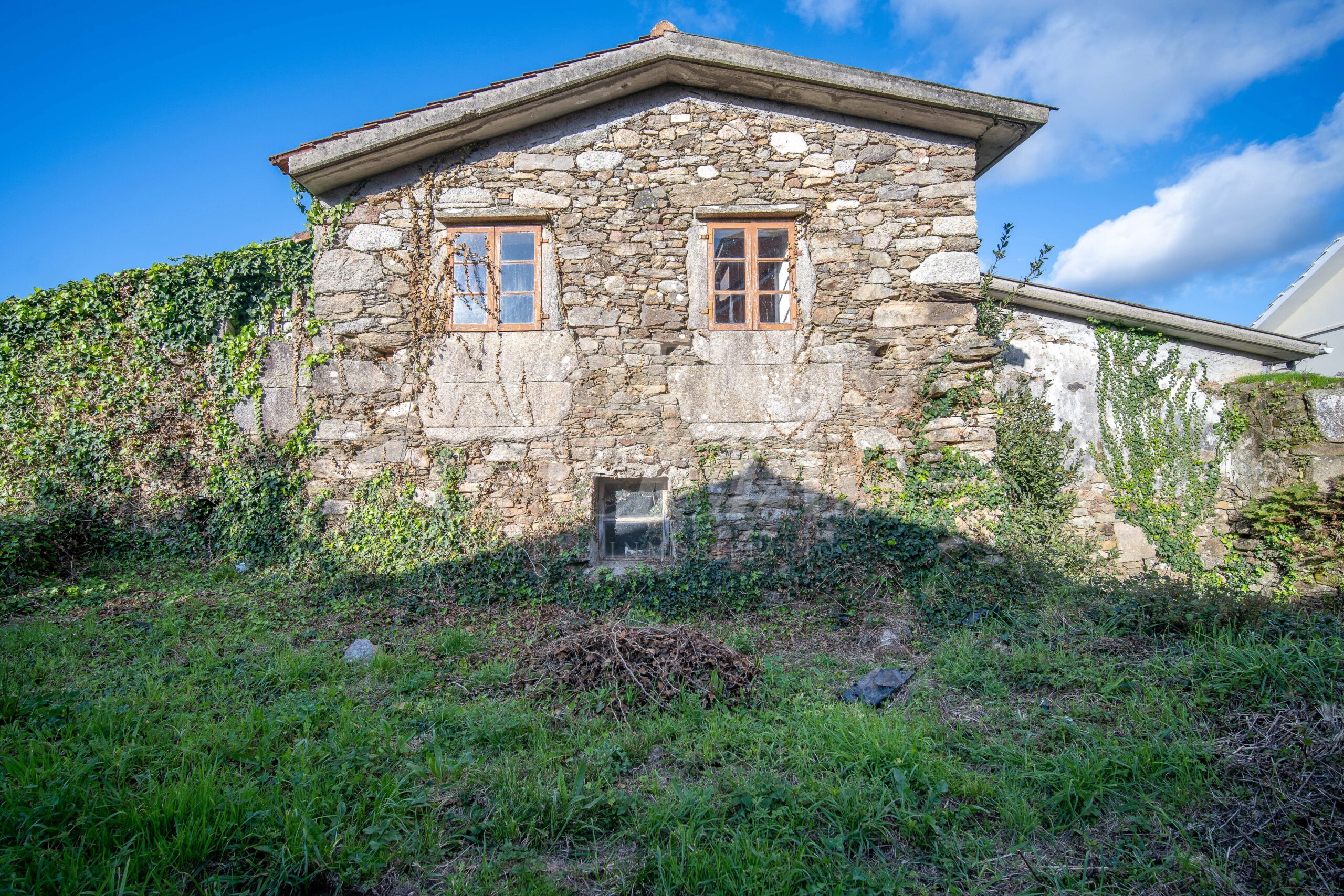 Vista general de la casa de piedra para rehabilitar en Cabana de Bergantiños, mostrando su arquitectura tradicional gallega y su ubicación en la aldea junto a otras viviendas